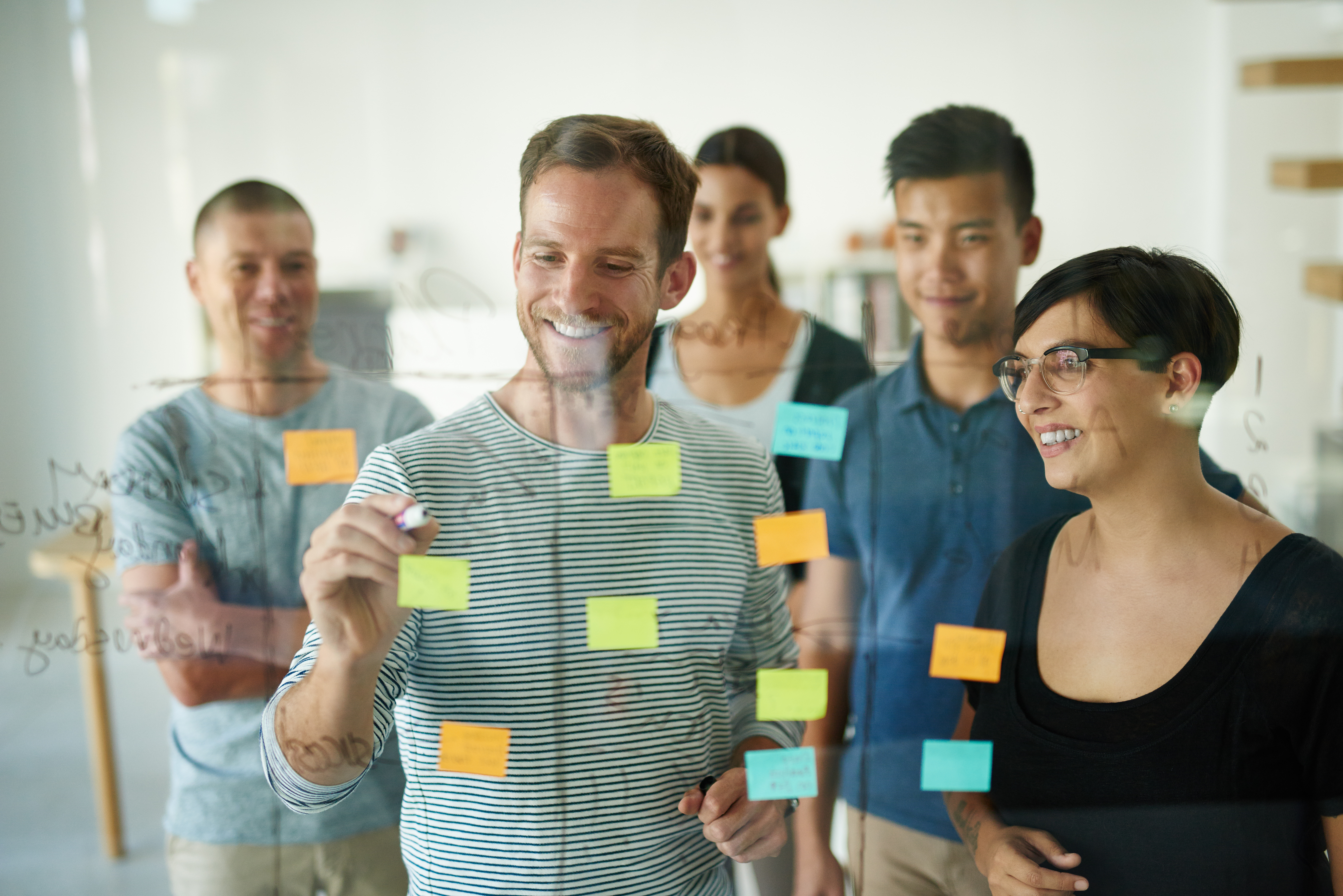 Eine Gruppe Menschen steht vor einer Glasscheibe, auf der Glasscheibe sind mehrere Post-Its angebracht